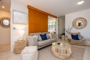 A modern living room with a sofa, two wicker chairs, a round coffee table, and a large mirror. - 1 Bright Point Apartment 1307 (Nelly Bay)