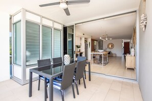 A modern dining area with a glass table and chairs, a ceiling fan, and a view into the kitchen. - 1 Bright Point Apartment 1307 (Nelly Bay)