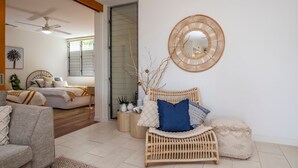 A living room with a sofa, a rattan chair, a round mirror, and a ceiling fan.