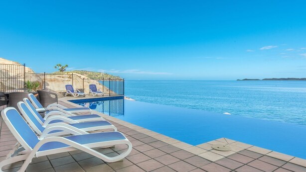An infinity pool with lounge chairs, a view of the sea, and a clear sky.