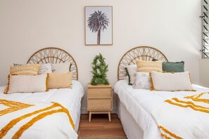 A bedroom with two beds, a nightstand, a framed picture, and a small plant. - 1 Bright Point Apartment 1307 (Nelly Bay)