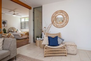 A living room with a sofa, a rattan chair, a round mirror, and a ceiling fan. - 1 Bright Point Apartment 1307 (Nelly Bay)