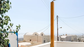 Un balcón con una mesa y sillas blancas, una planta en maceta y vistas de edificios a lo lejos.