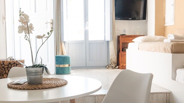 Una sala de estar moderna con un sofá blanco, una mesa de comedor con sillas y un televisor montado en la pared.
