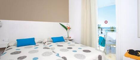 A hotel room with a bed, a small table with a plant, and a view of the outside balcony.