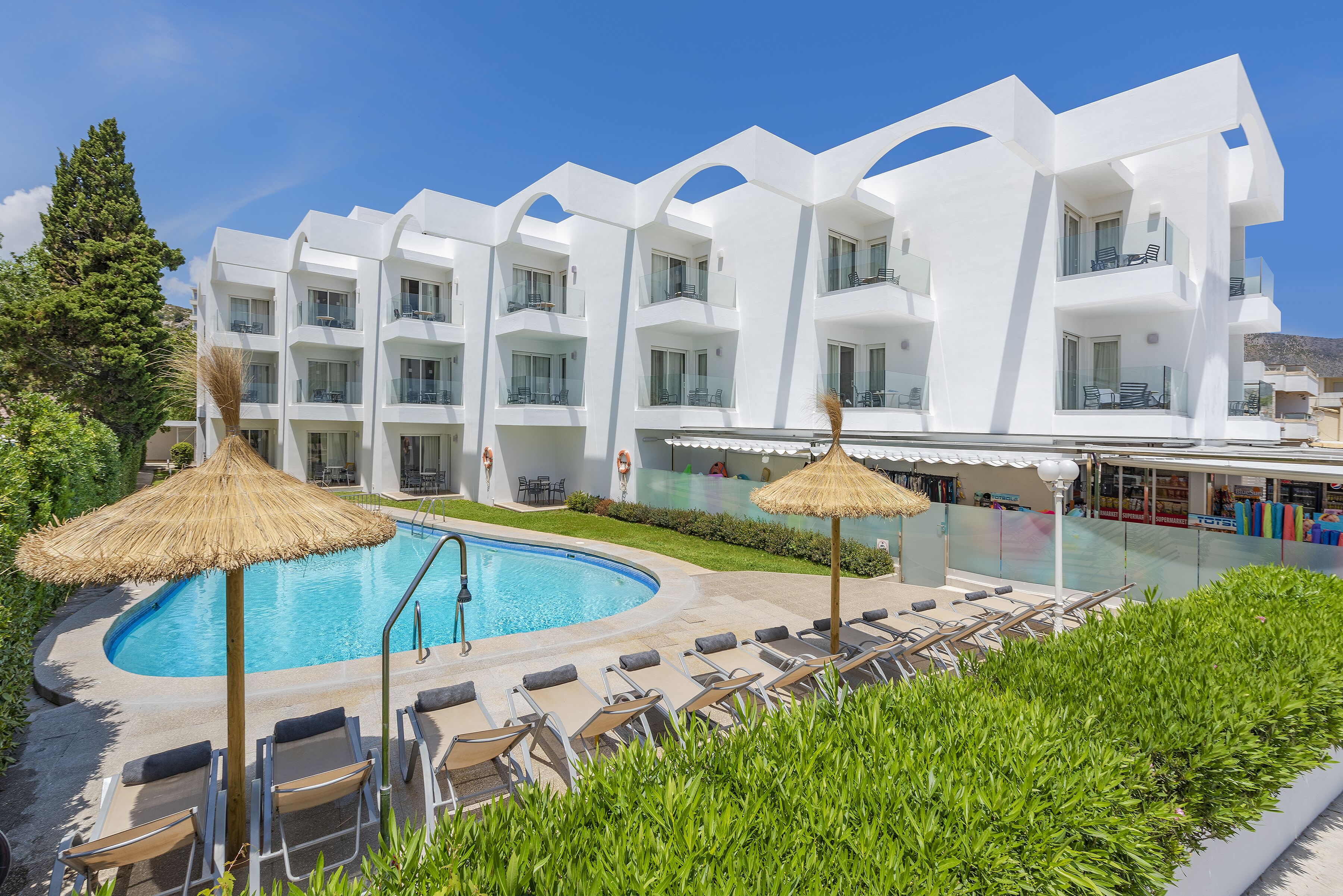 A modern hotel with a swimming pool, sun loungers, and a thatched umbrella.