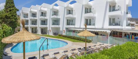 A modern hotel with a swimming pool, sun loungers, and a thatched umbrella.