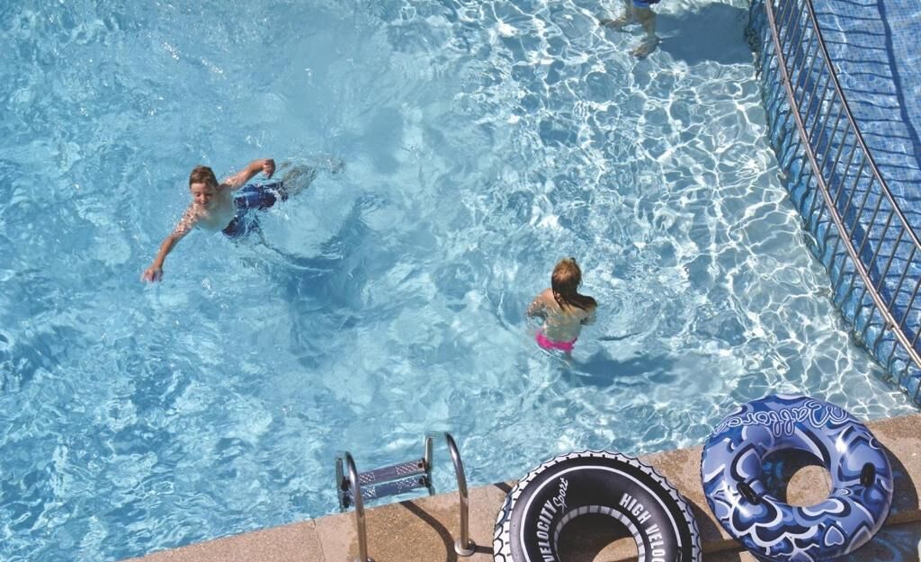 En swimmingpool med klart vand, en stige og en blå oppustelig flyder.