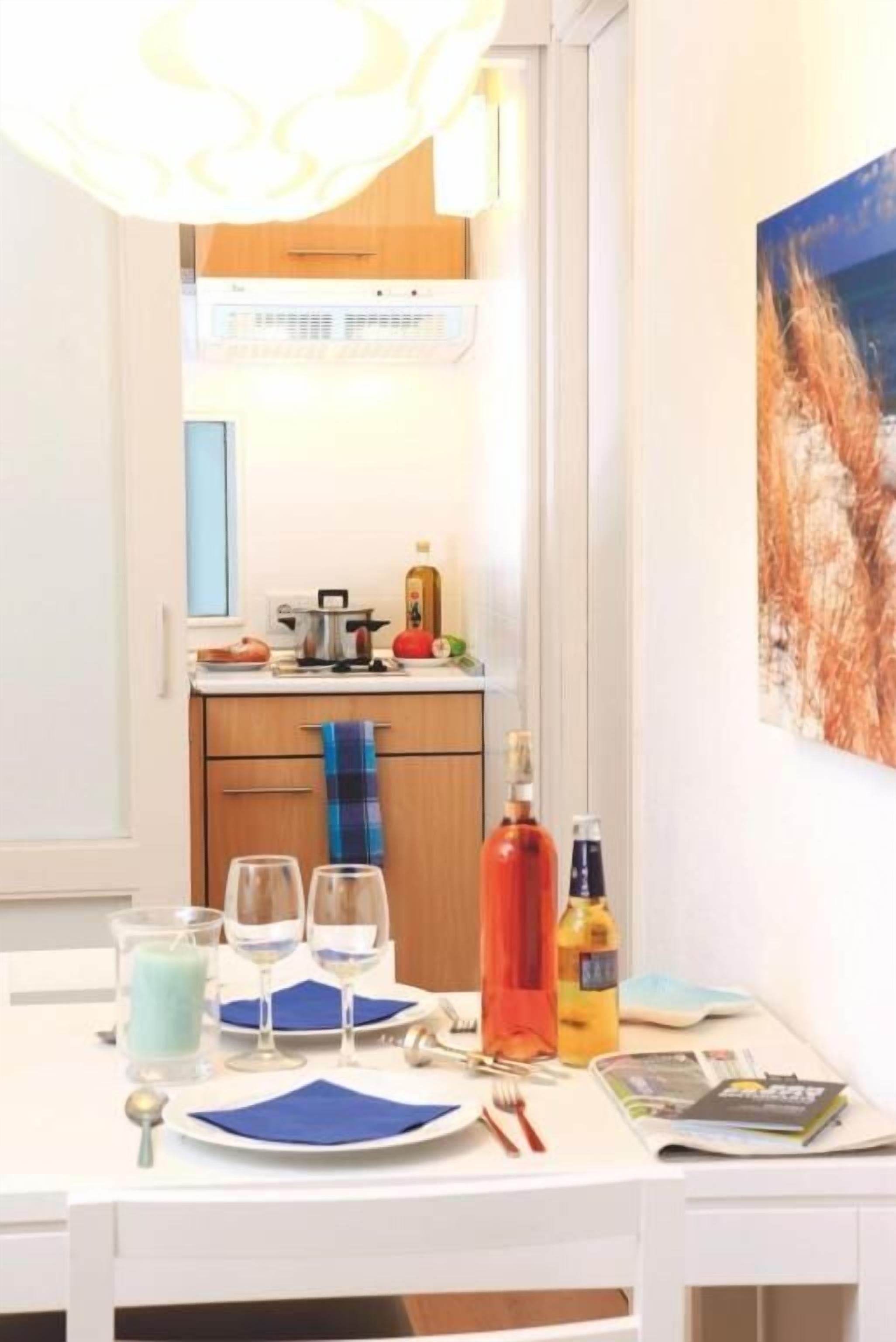 Ein Essbereich mit einem Tisch für zwei Personen, eine Küche im Hintergrund und ein Gemälde an der Wand.