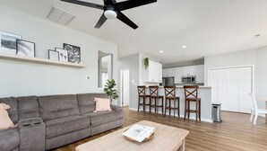 Ein modernes Wohnzimmer mit grauem Sofa, Couchtisch aus Holz und Deckenventilator.