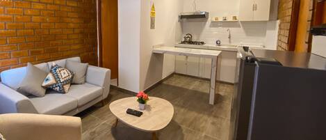 A compact living space with a sofa, a coffee table, a kitchen area with a stove, cabinets, and a refrigerator.