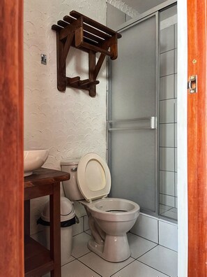 A bathroom with a toilet, a wooden shelf, and a glass shower enclosure.