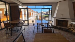 A spacious patio with a stone floor, wooden tables and chairs, and a large glass door leading to an outdoor area with a view of buildings and mountains. - Tupac Hostel Huaraz (Huaraz)