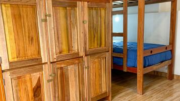 Un lit superposé avec une literie bleue, une armoire en bois à plusieurs portes et un tapis à motifs sur un plancher en bois.