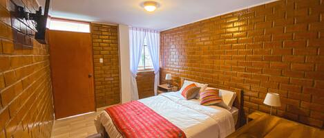 Un dormitorio con pared de ladrillo, cama de madera, mesita de noche y ventana con cortinas.