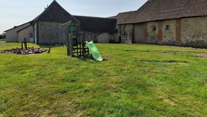 Une cour verdoyante avec une structure de jeux pour enfants et un bâtiment doté d’un toit en tuiles.
