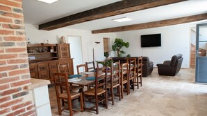 Un espace repas avec des chaises et des tables en bois, un mur en briques, un téléviseur et un escalier.