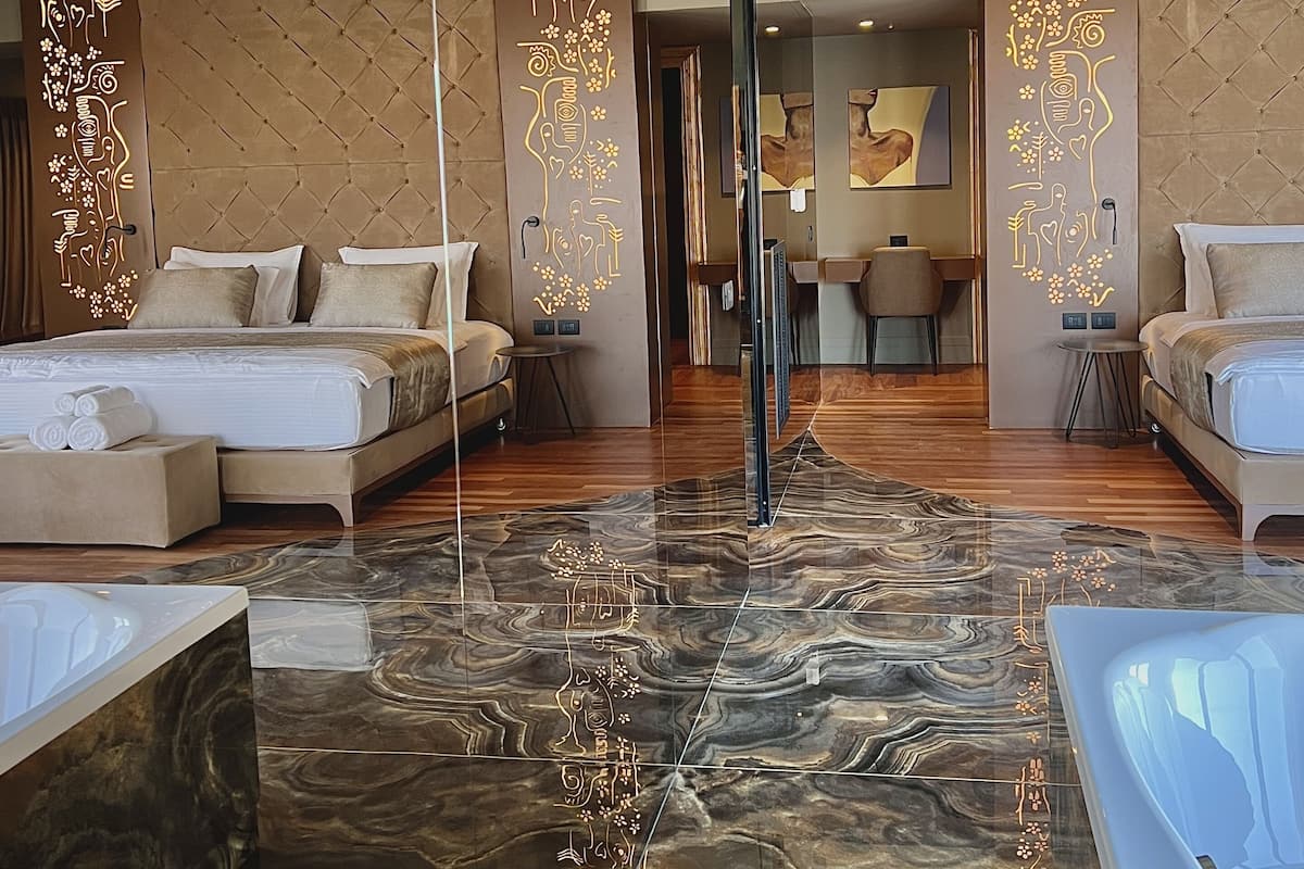 Une chambre d’hôtel moderne dotée d’un grand lit, d’un coin salon séparé et d’un sol en marbre.