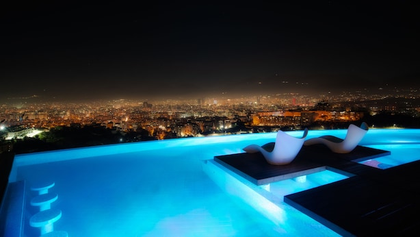 A rooftop infinity pool with two lounge chairs and a cityscape view at night. - Arka Art Hotel  (Farkë)