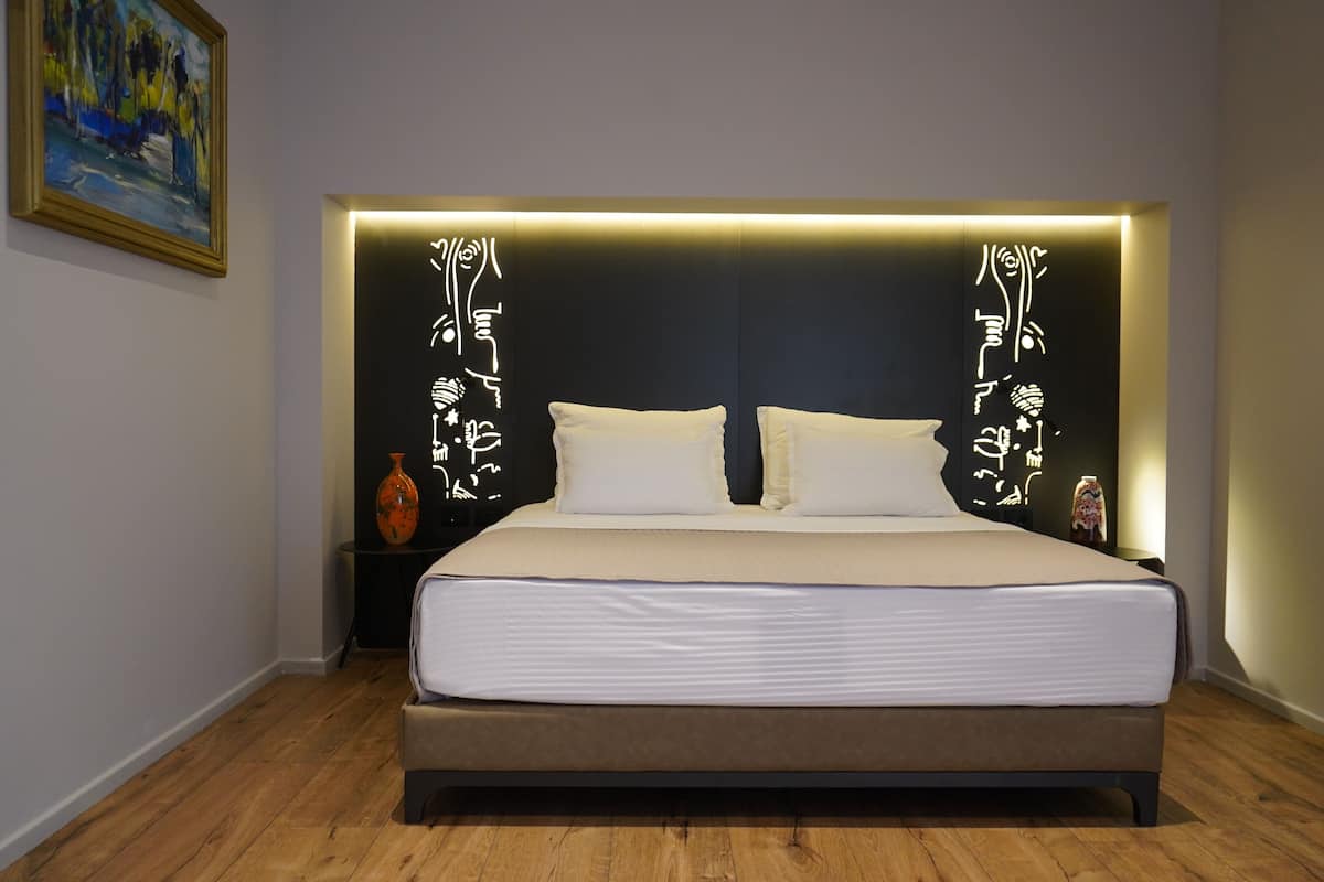 Une chambre à coucher moderne avec un grand lit, une tête de lit ornée de motifs lumineux et une petite table sur laquelle est posé un vase.