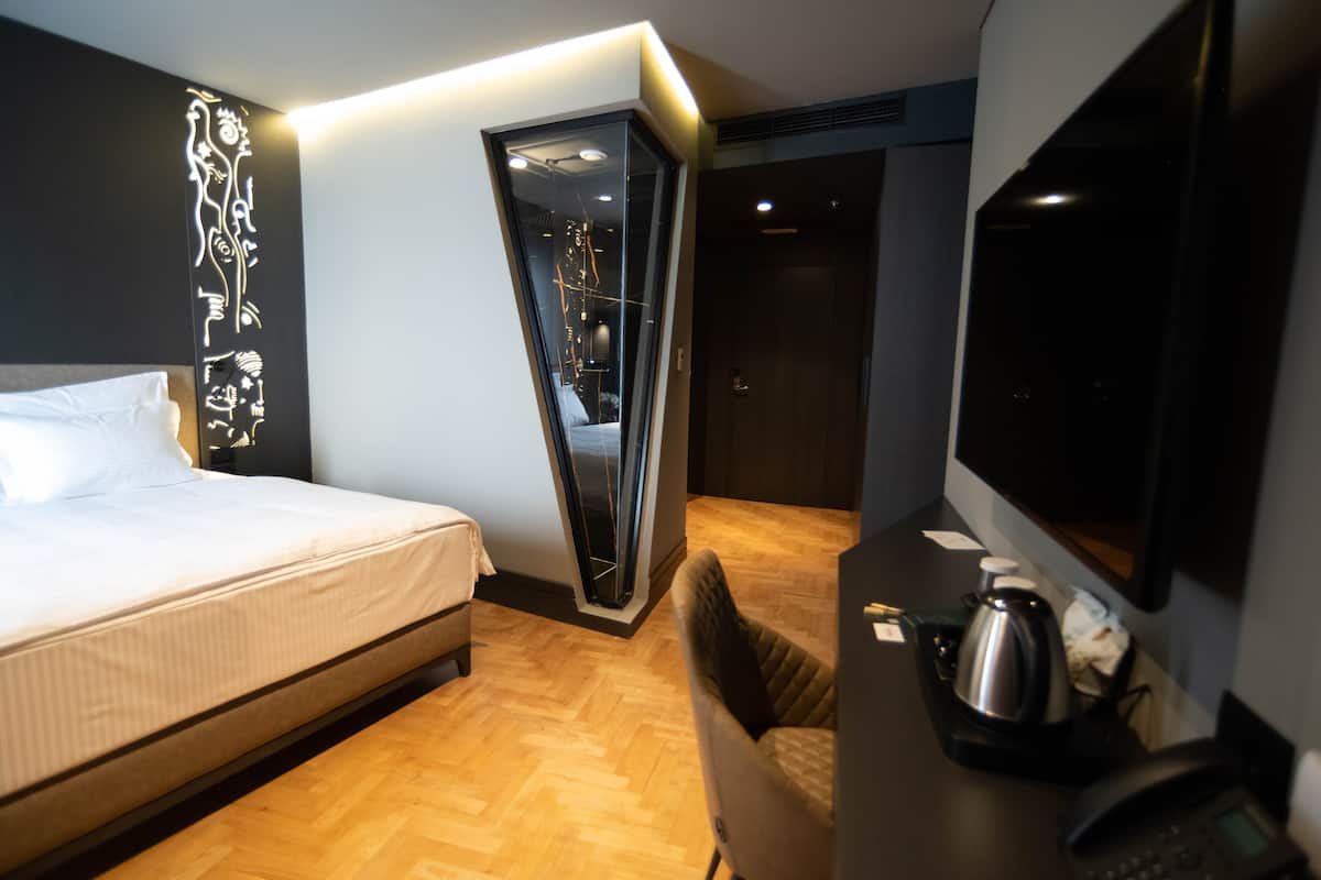 Une chambre d’hôtel moderne équipée d’un lit, d’un bureau avec une machine à café, d’une télévision et d’une œuvre d’art murale originale.