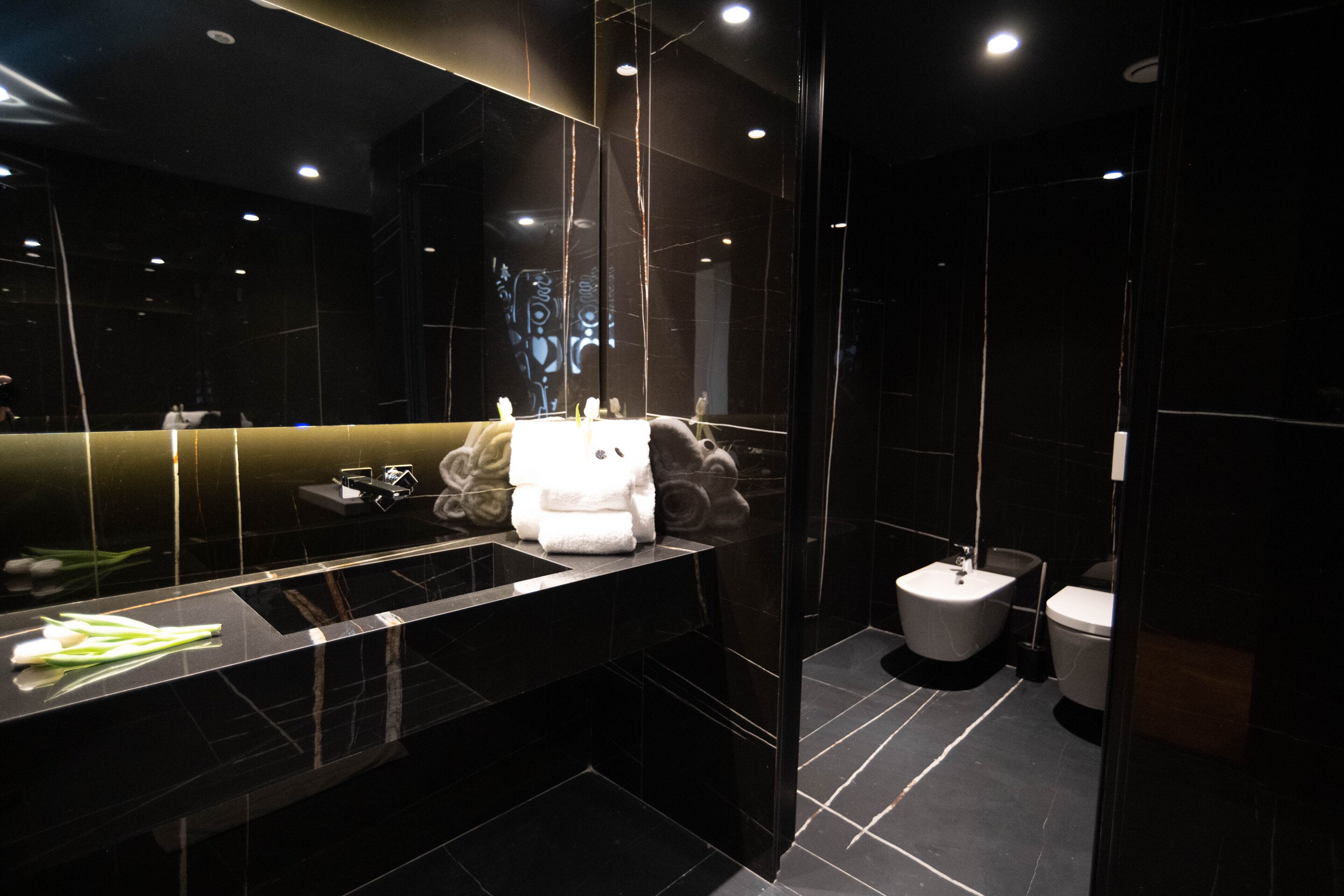 A modern bathroom with a black marble sink, a large mirror, and a toilet.