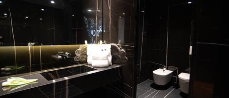 A modern bathroom with a black marble sink, a large mirror, and a toilet.