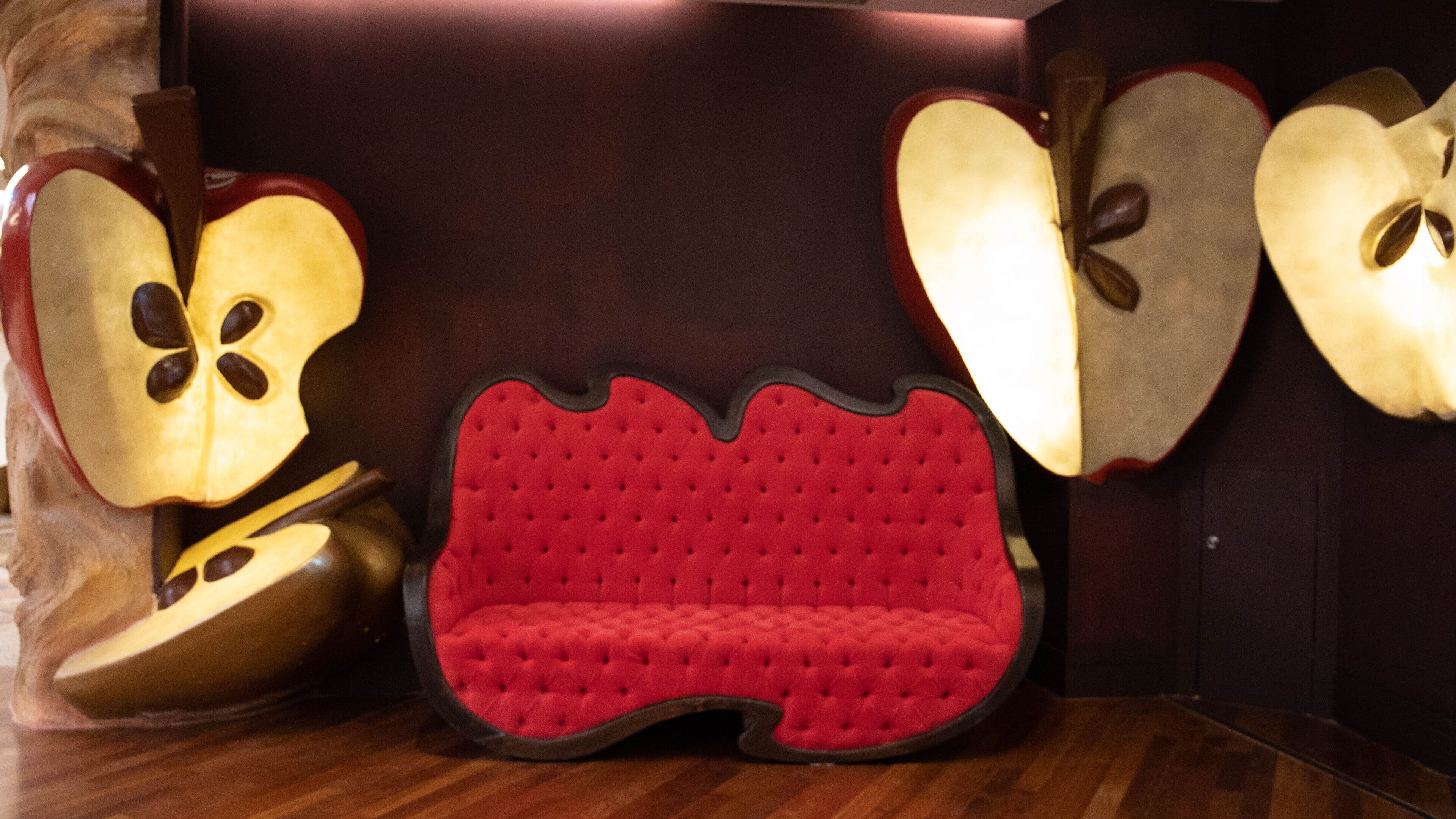 A room with a red tufted sofa, large apple-shaped sculptures, and a wooden floor.
