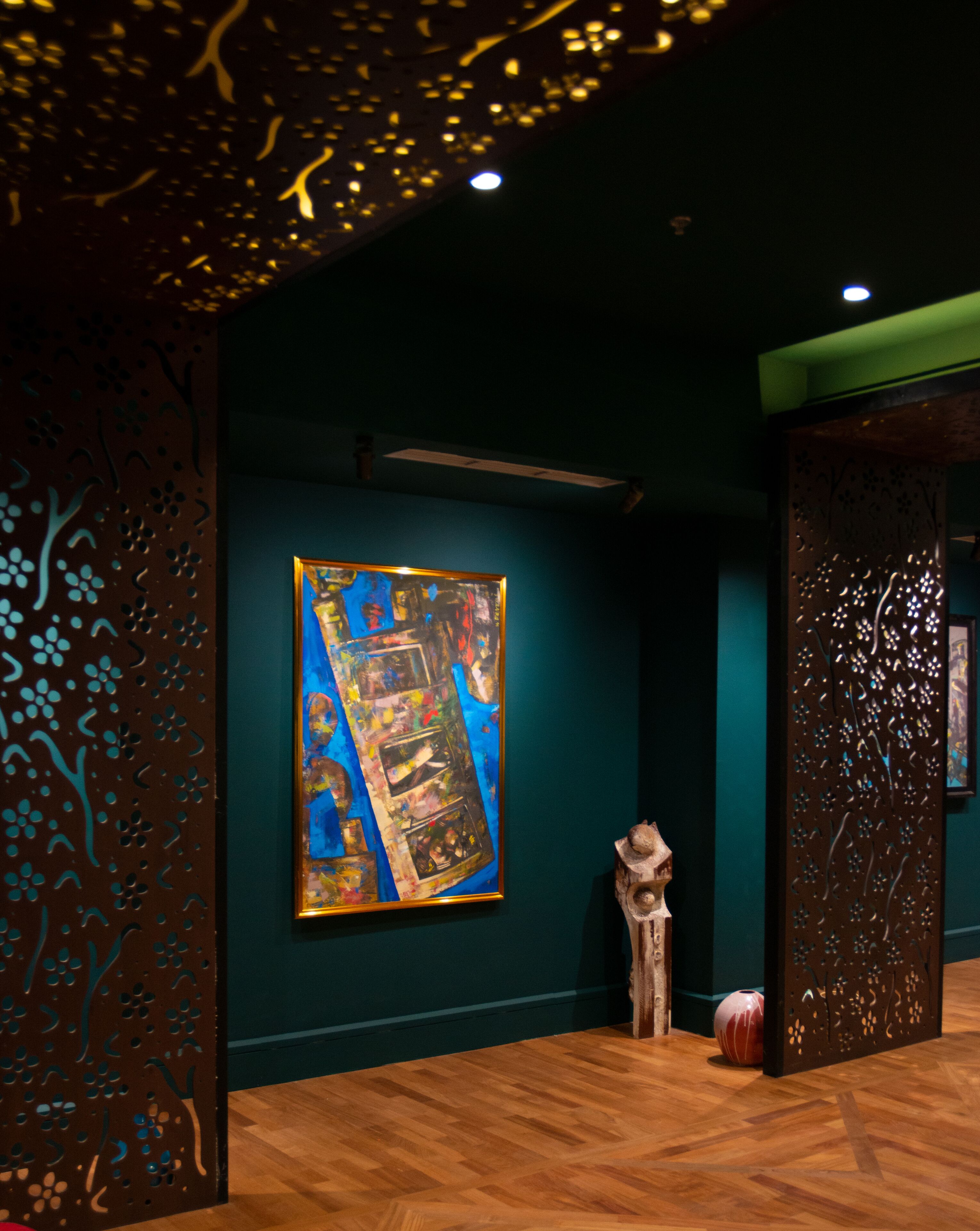 Een kunstgalerie met een groot abstract schilderij aan de muur, houten vloeren en decoratieve panelen.