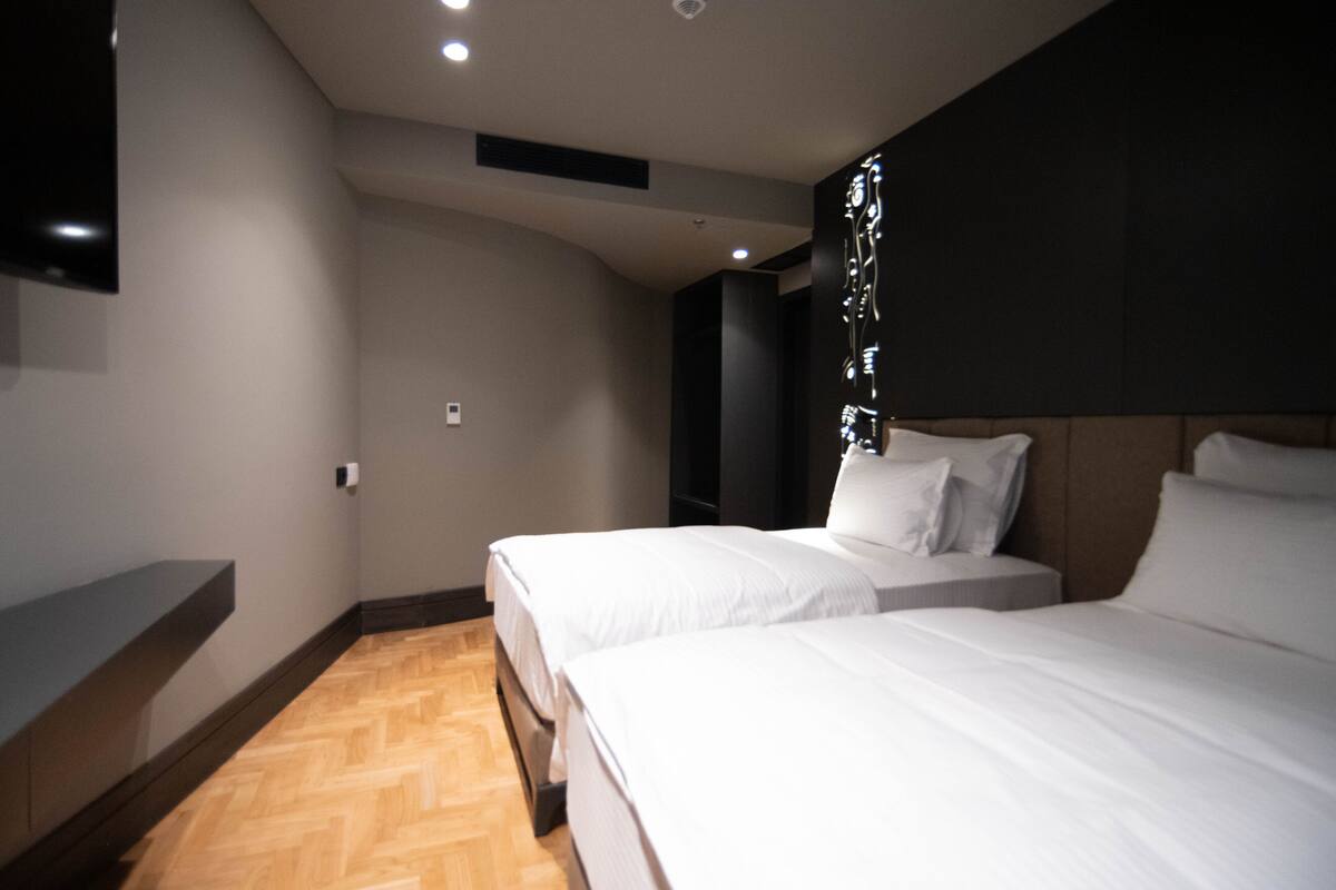 Une chambre d’hôtel avec deux lits, un téléviseur à écran plat fixé au mur et un plancher en bois.
