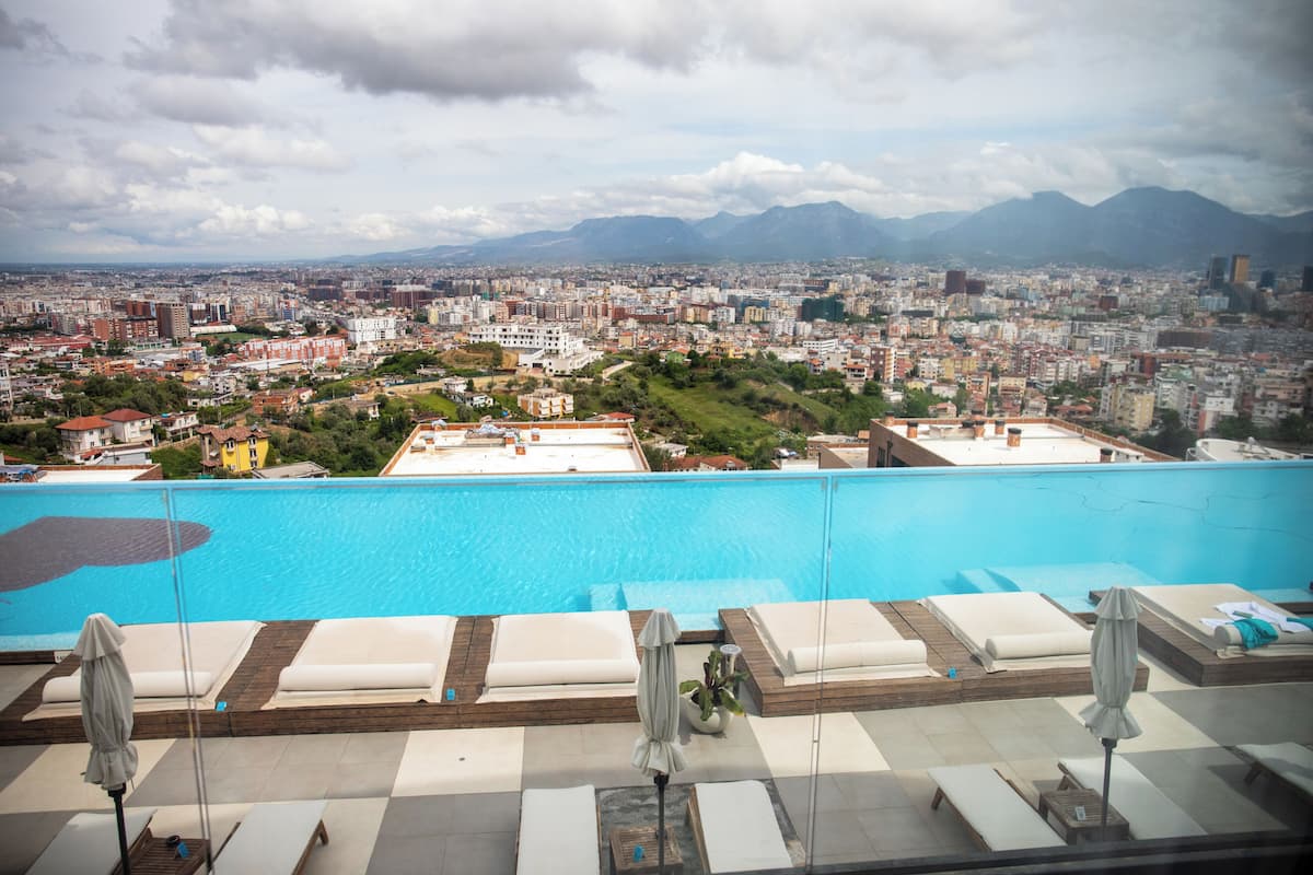 Un espace piscine aménagé sur le toit, avec des chaises longues et des parasols, offrant une vue sur le paysage urbain et les montagnes en arrière-plan.