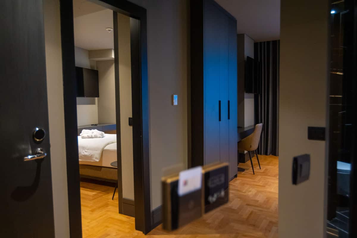 Une chambre d’hôtel avec un lit, un bureau et une chaise. Une porte donne accès à une autre pièce.