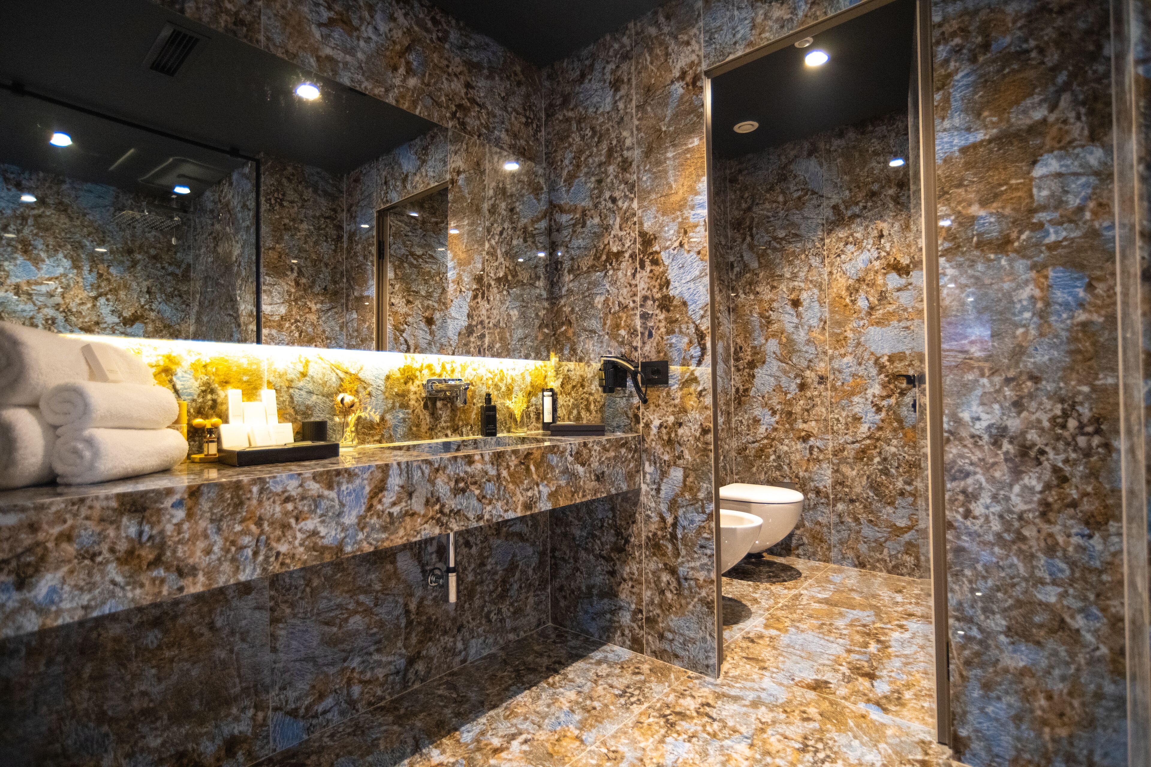 A modern bathroom with a marble vanity, a large mirror, and a glass-enclosed shower area.