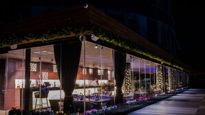 A restaurant with a glass enclosure, outdoor seating, and decorative lights. - Arka Art Hotel  (Farkë)