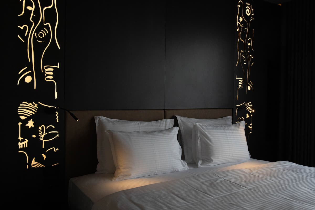 Une chambre moderne avec un grand lit, une tête de lit sombre et des œuvres d’art décoratives au mur.