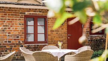 An outdoor seating area with wicker chairs and a table, a brick wall, and a red door.