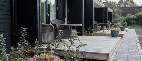 A modern outdoor seating area with wicker chairs and a table, surrounded by potted plants and flowers.