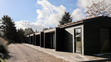 A row of modern cabins with large sliding doors, a gravel path, and a backdrop of trees and a clear sky.