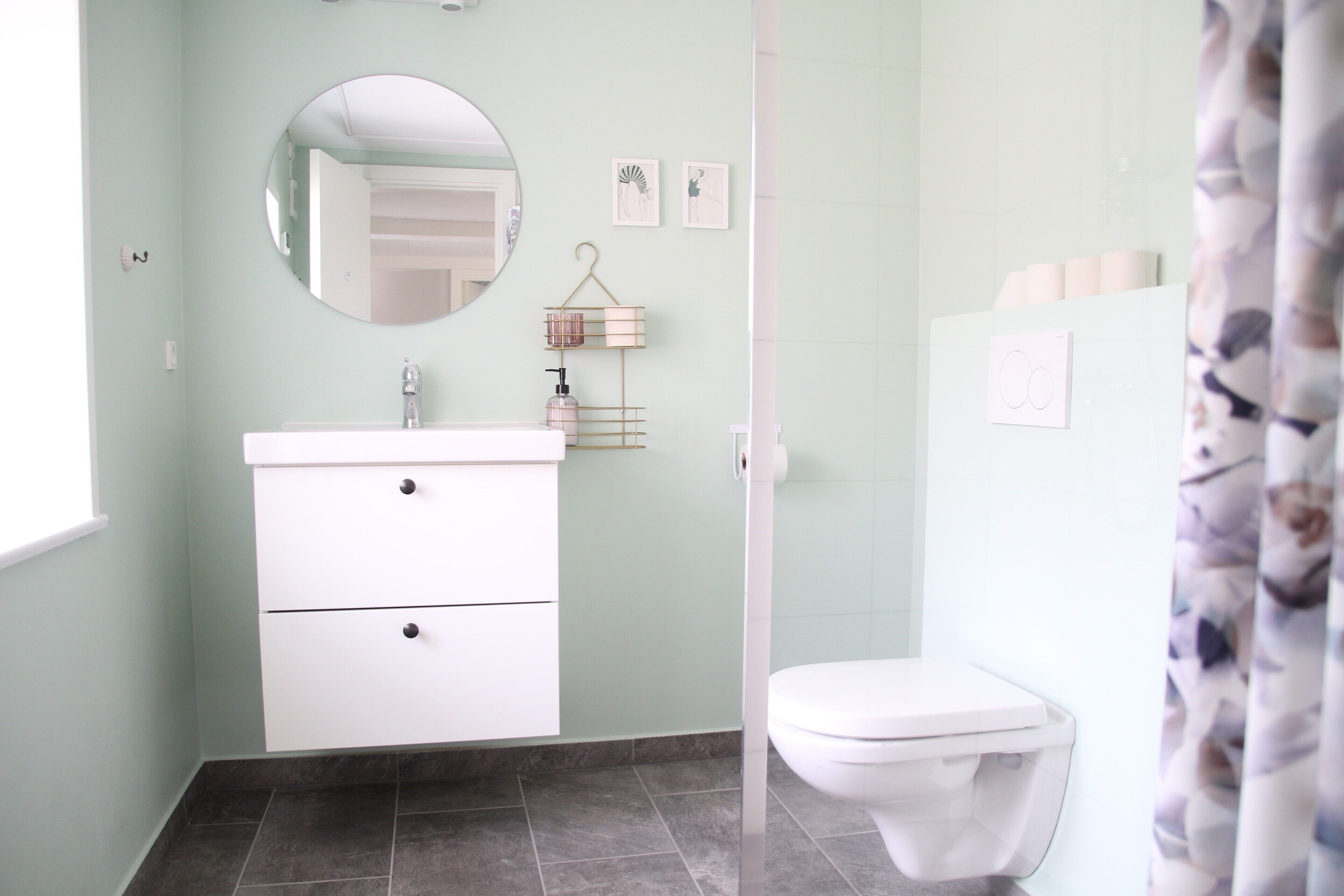 A bathroom with a white vanity, a round mirror, a toilet, and a shower curtain.