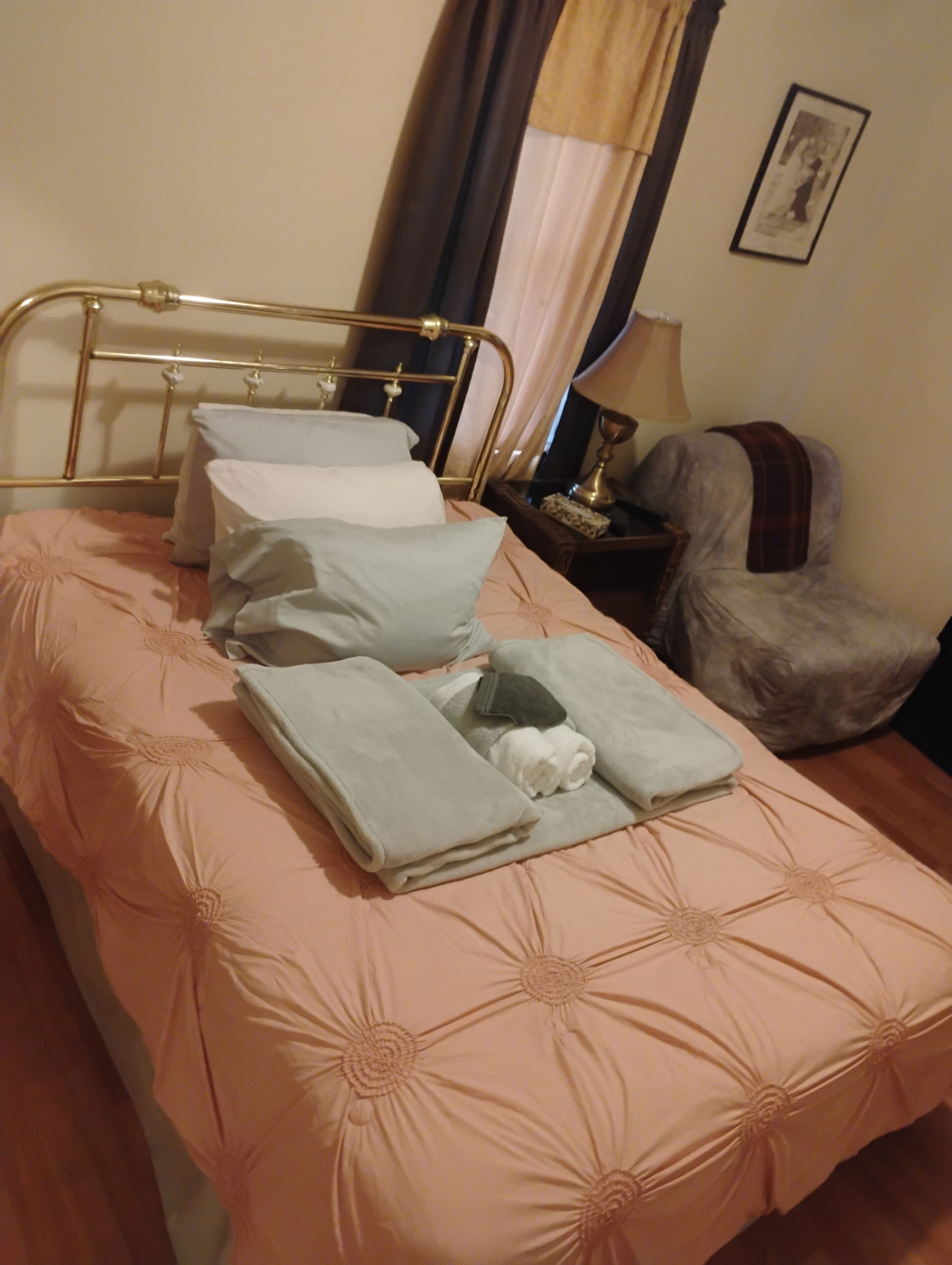 A neatly made bed with a metal frame, a bedside table with a lamp, and a chair with a blanket.