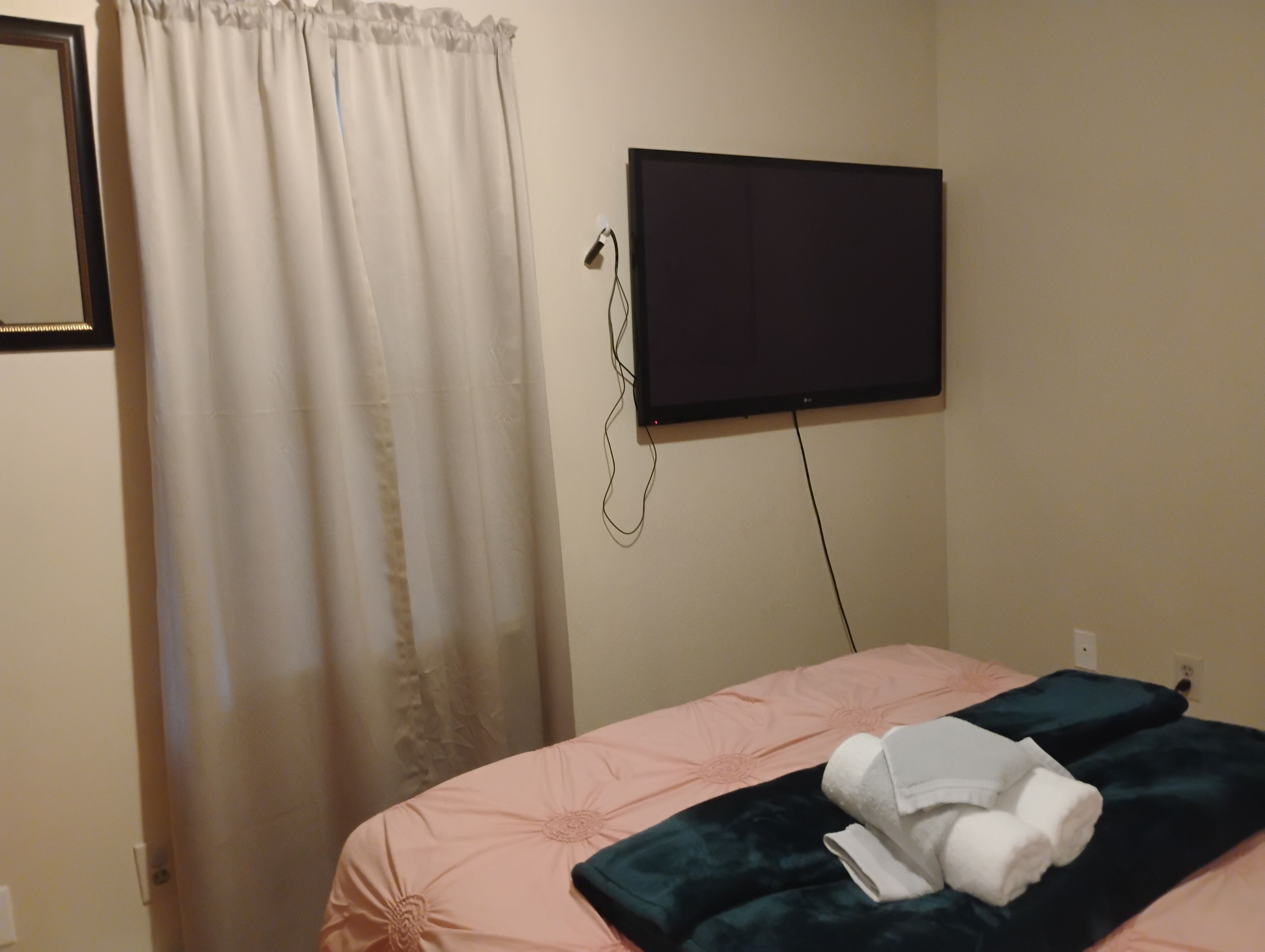 A hotel room with a bed, a flat-screen TV mounted on the wall, and a curtain.