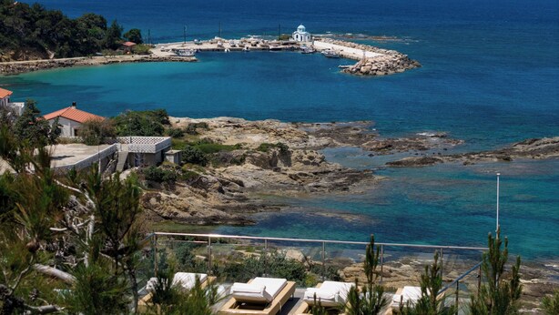 Un hotel frente al mar con terraza, un faro y aguas azules cristalinas.