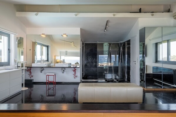 Una cocina moderna con una isla central, cabina de ducha con mampara de vidrio y un espejo grande que refleja el ambiente.