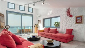 Una sala de estar moderna con un sofá rojo, una mesa de centro redonda y vista al mar a través de amplios ventanales.