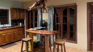 Een keuken met houten kastjes, een ronde eettafel, twee krukken en een hangende lamp.