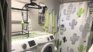 Un área de lavandería con dos lavadoras de carga frontal, un tendedero y una cortina de ducha con diseño de cactus.