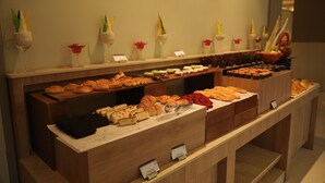 Um buffet com diversos pastéis e sobremesas, incluindo croissants, bolos e pão.