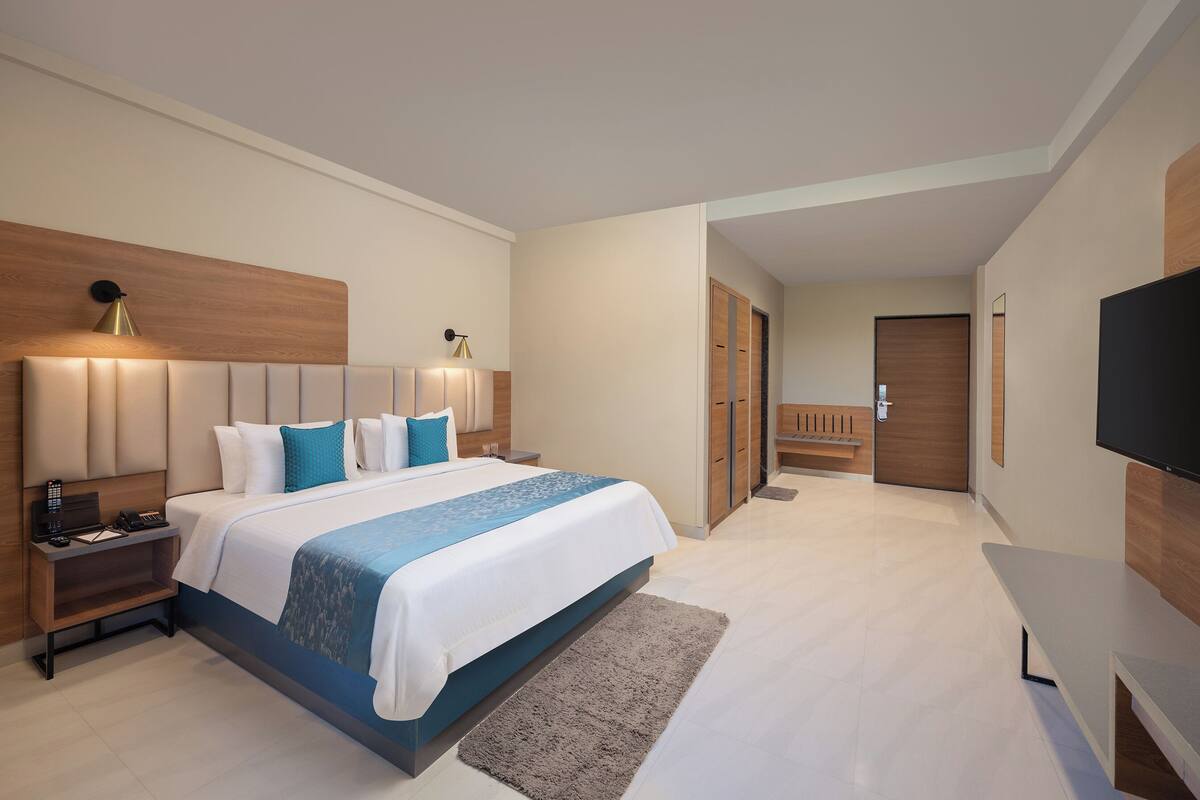 A modern hotel room with a large bed, bedside tables, a TV, and a wardrobe.