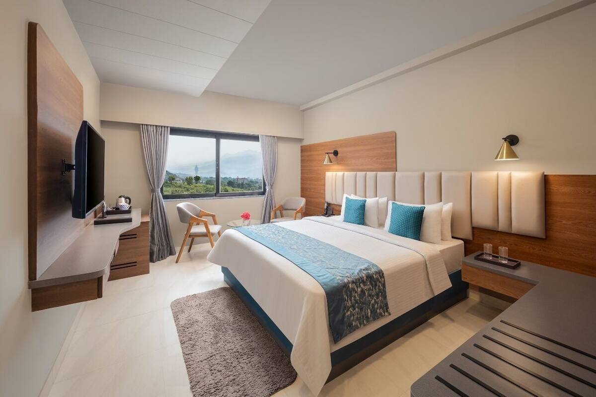 A modern hotel room with a large bed, a TV, a desk, and a view of the outdoors.