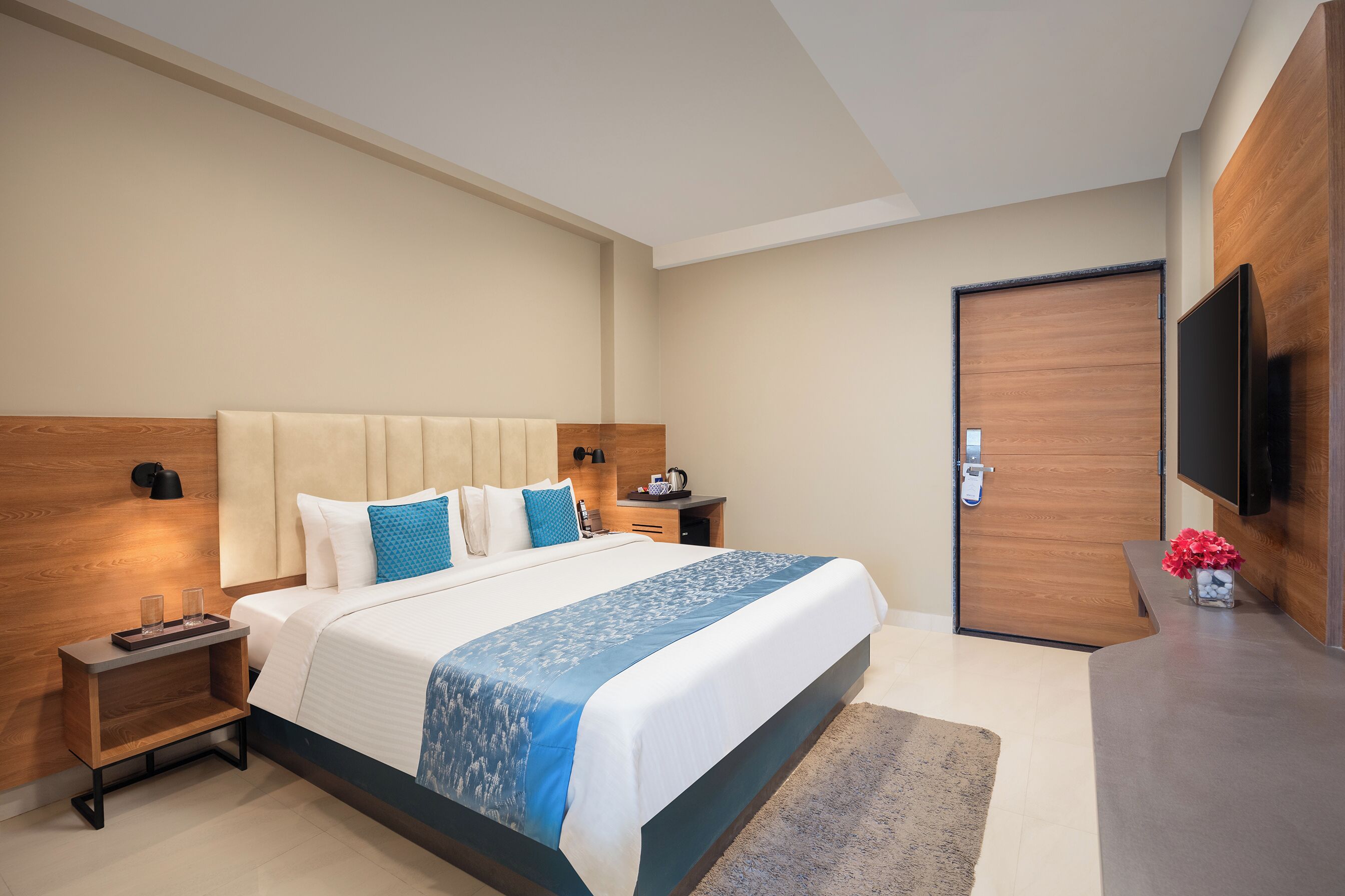 A modern hotel room with a large bed, bedside tables, a flat-screen TV, and a wooden door.